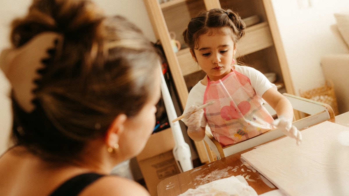 A woman watches a child playing with flour.